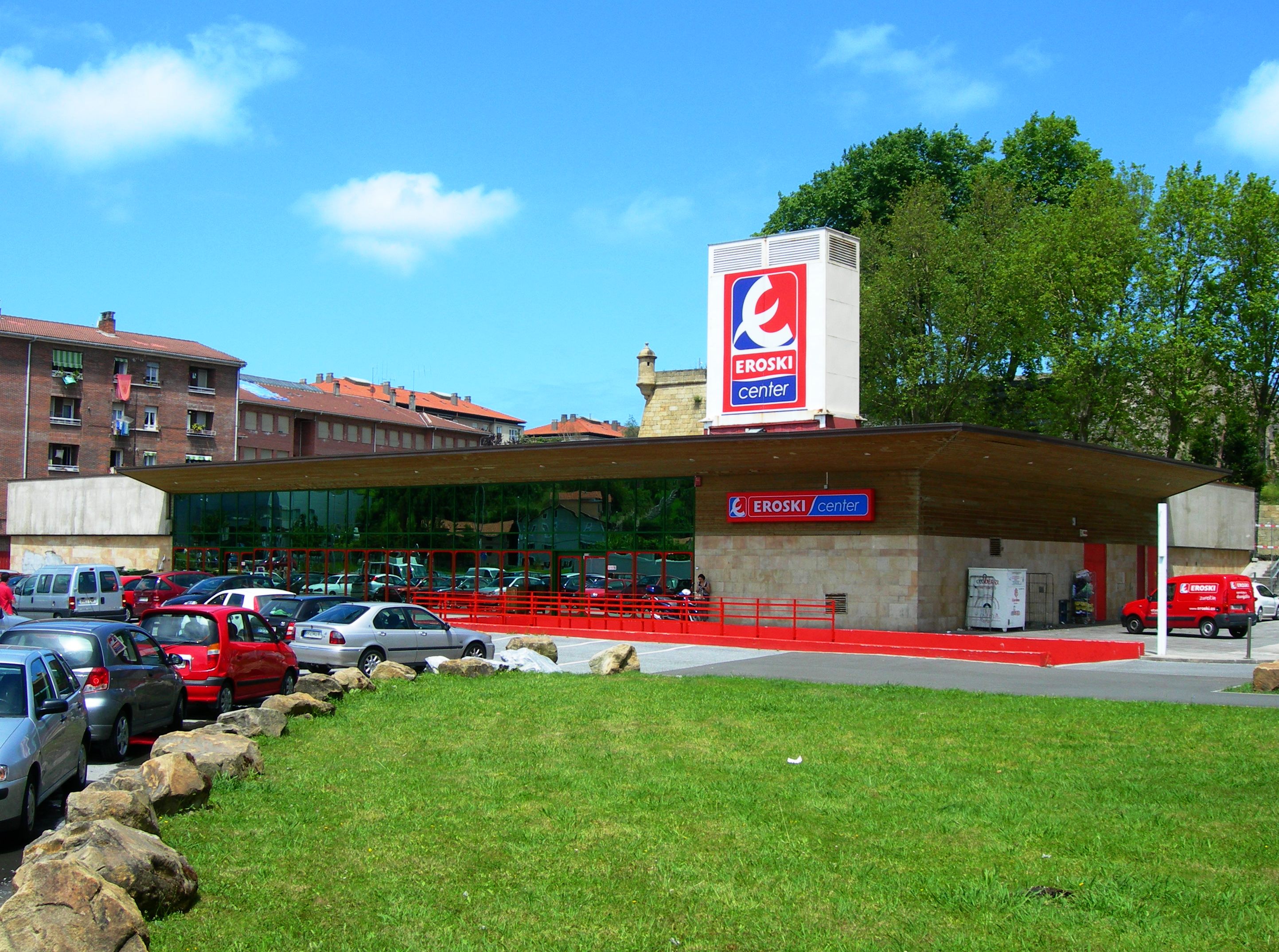 A grocery store belonging to Eroski S.p.A with a vibrant green lawn and blue sky