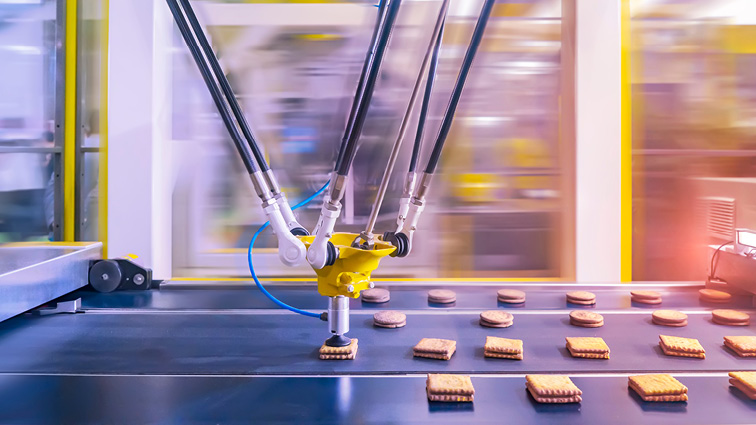 A robotic arm makes sandwich cookies on a conveyer belt
