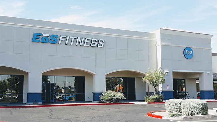 The facade of an EoS Fitness building, with a gray exterior, arched entrances and a blue sky.