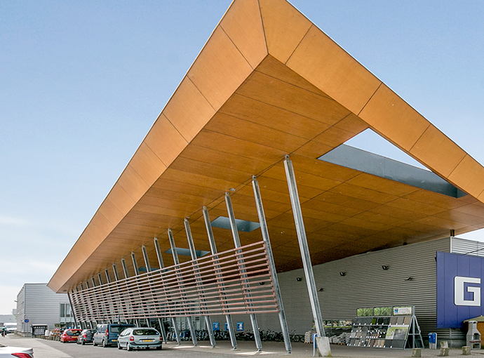 The outside of a building owned by W. P. Carey, with a large wooden architectural roof and cars lined up outside.