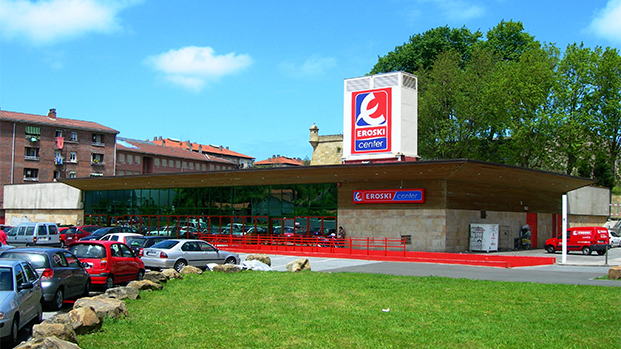 A grocery store belonging to Eroski S.p.A with a vibrant green lawn and blue sky