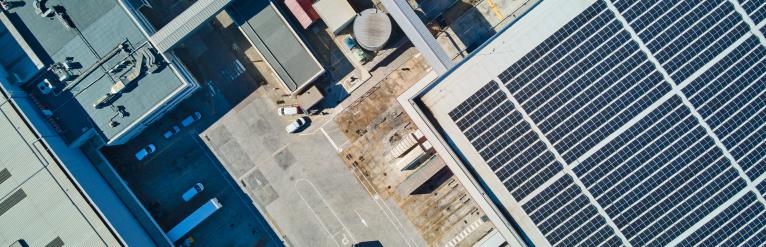 Aerial view of a warehouse with solar panels next to a parking lot filled with cars and trucks.