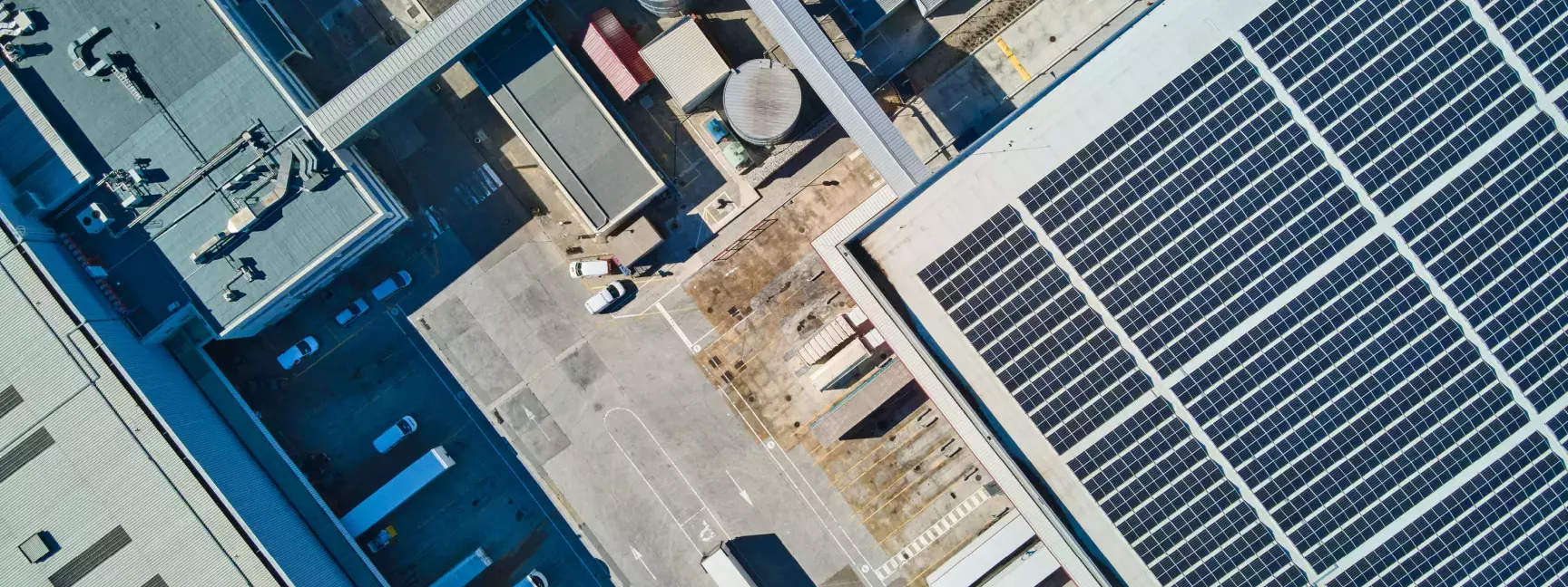 Aerial view of a warehouse with solar panels next to a parking lot filled with cars and trucks.